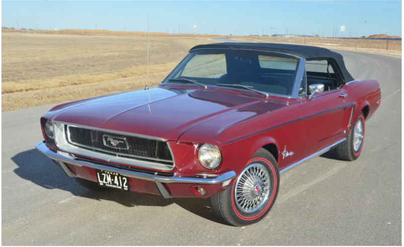 A red ford mustang convertible on a road between brown grass fields