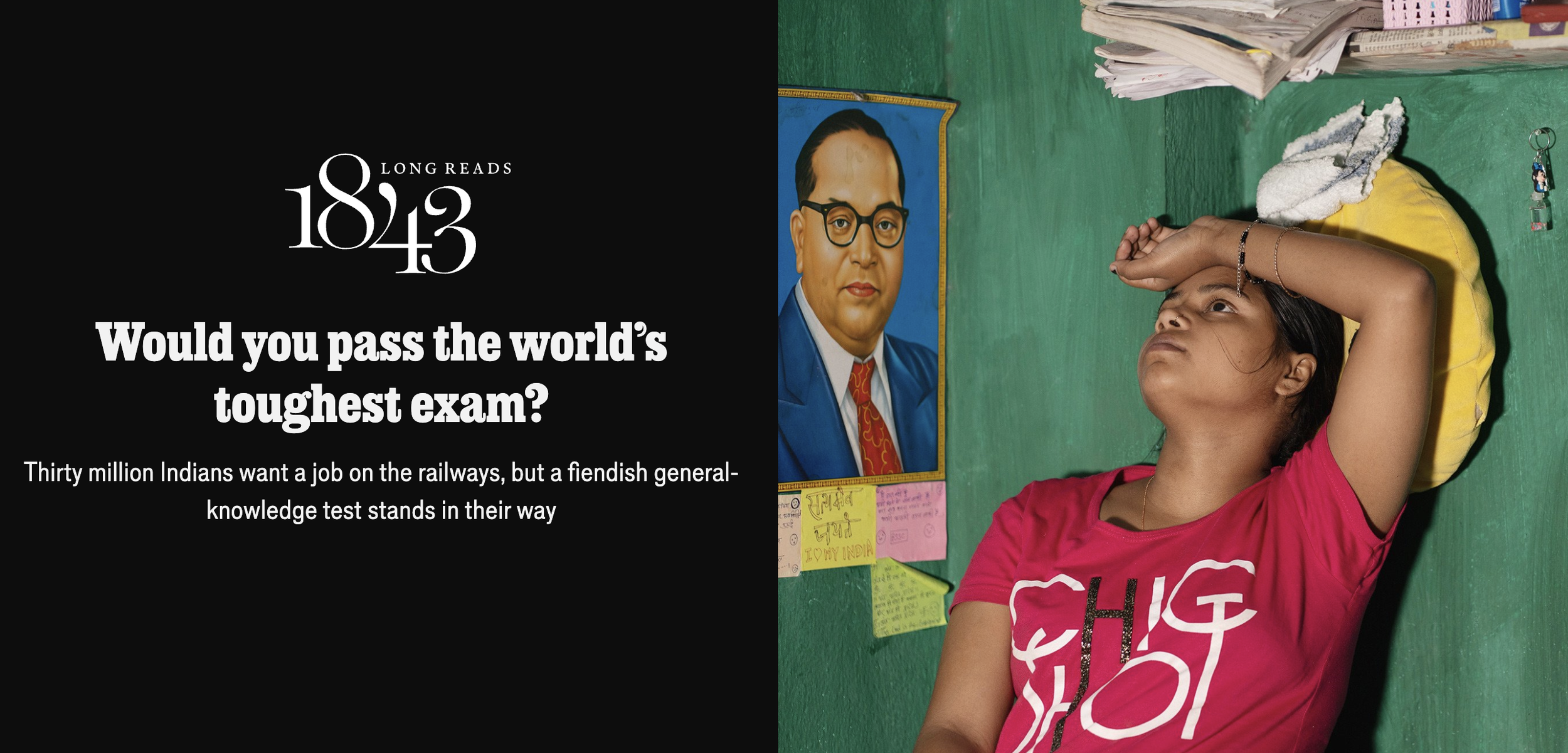 A young girl wearing a pink t-shirt with a graphic design, lying on a yellow pillow on the floor.  Behind her, a green wall features a framed portrait of a man with glasses, and colourful notes and papers are stuck on the wall.