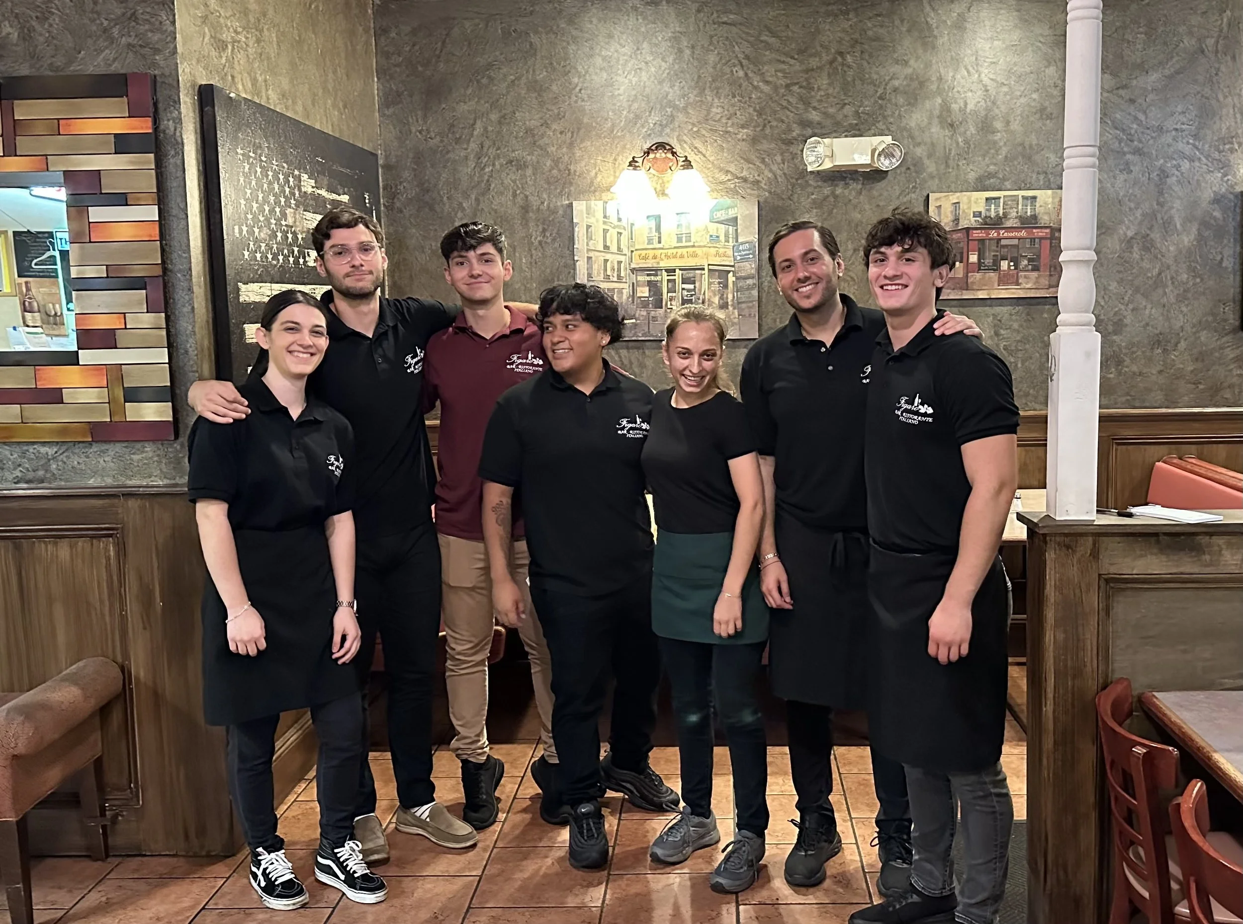Group of seven restaurant staff members standing in a restaurant, smiling and posing together.