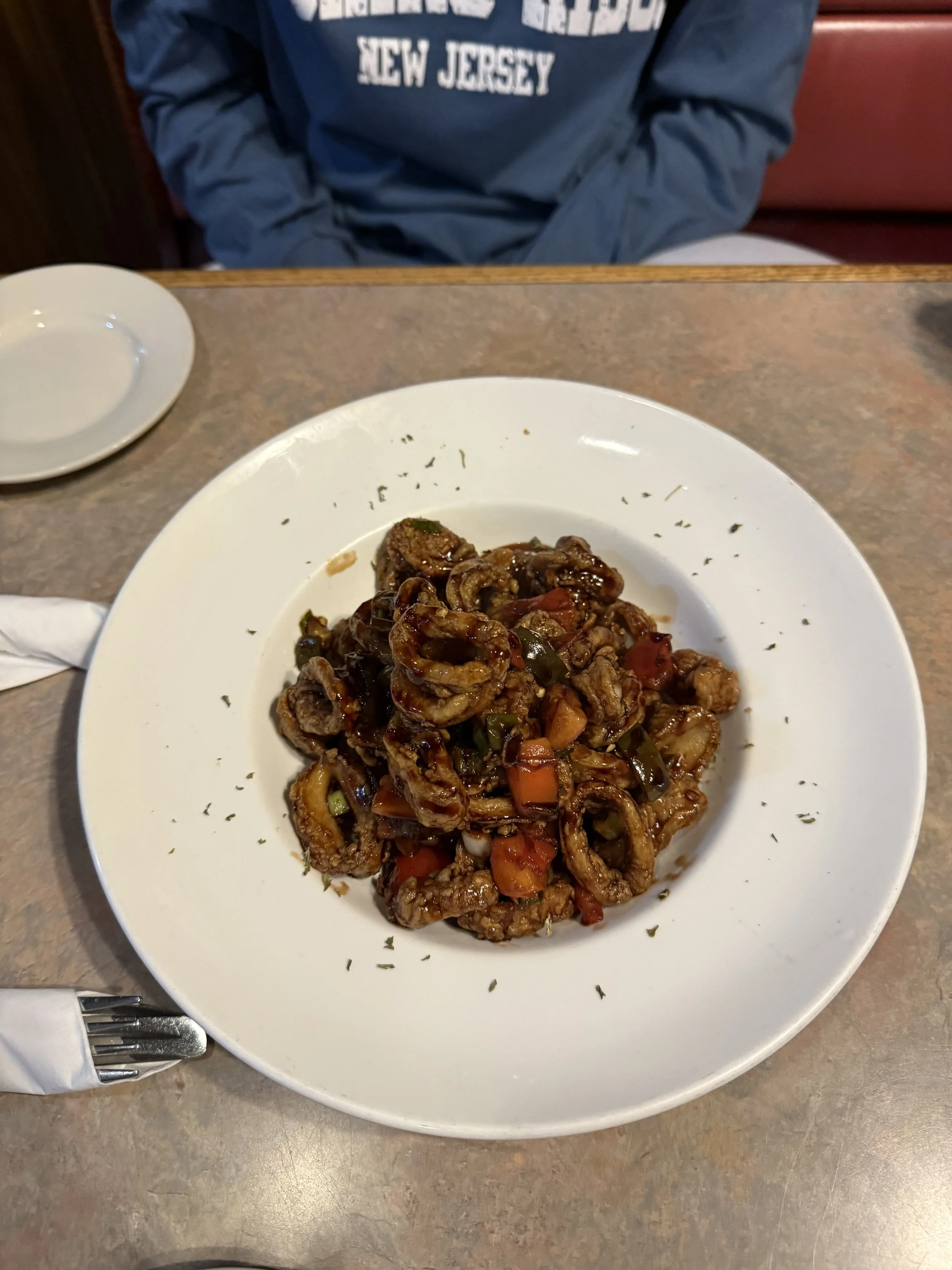 A plate of stir-fried beef with vegetables, including carrots and peppers, garnished with herbs, on a white plate on a brown table.