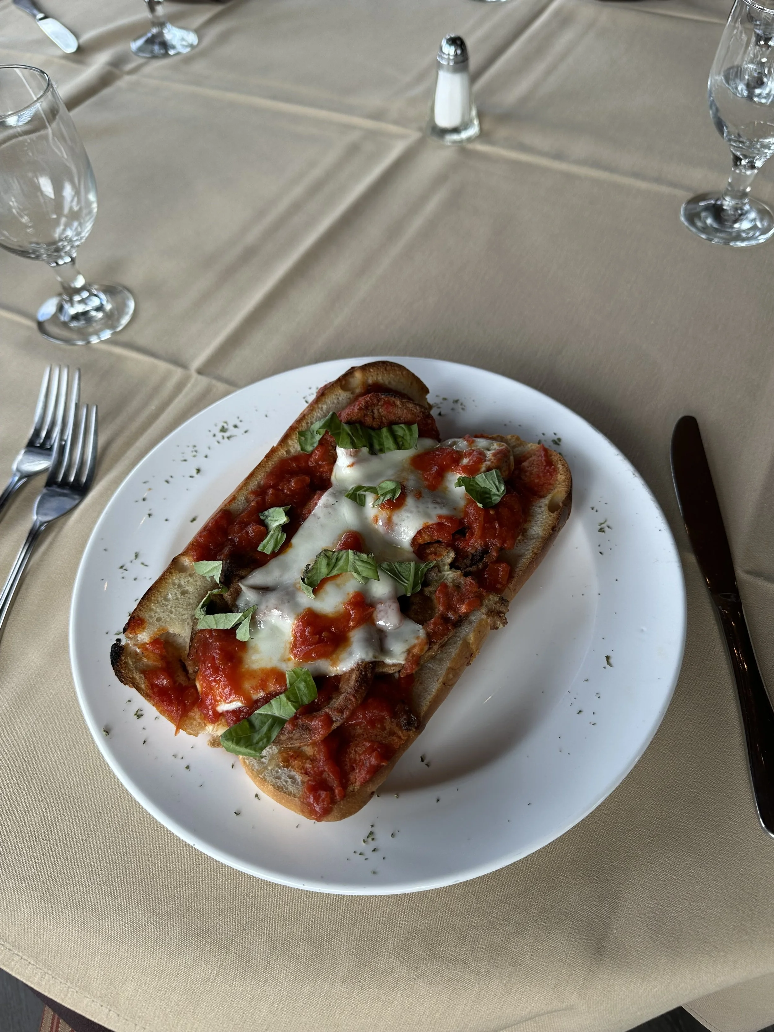Plate of baked Italian bread topped with melted cheese, tomato sauce, pieces of sausage, and fresh basil, on a white plate.