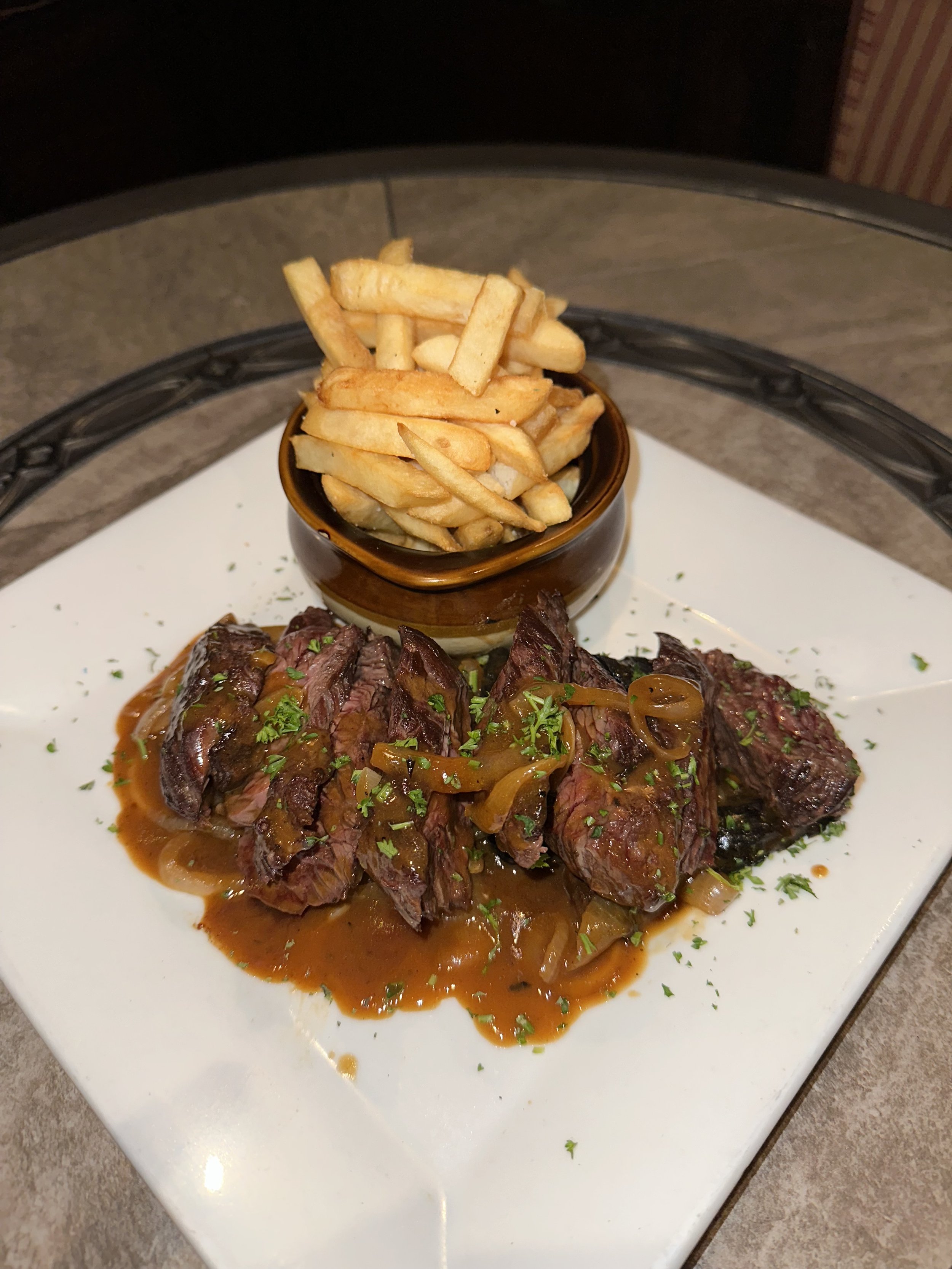 Steak with onion gravy, served with French fries in a small brown bowl on a white square plate.