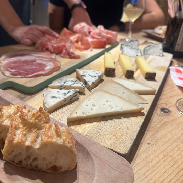 A cheese and charcuterie board with various cheeses, cured meats, and bread, served on a wooden table at a social gathering.