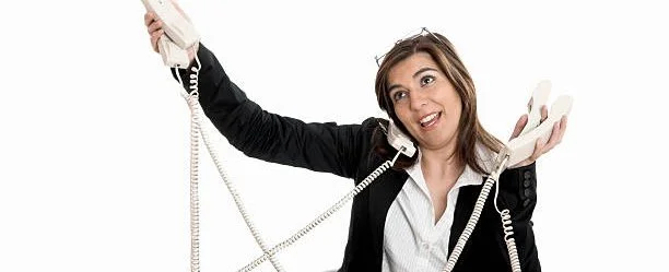 Woman holding multiple telephones and talking on one of them, appearing overwhelmed or busy.