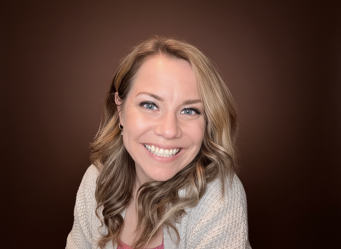 A woman with long, curly blonde hair smiling at the camera, wearing a light-colored sweater against a brown background.