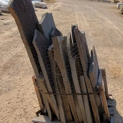 A wooden pallet holding various stones or slate slabs secured with wire, placed outdoors on a dirt surface.