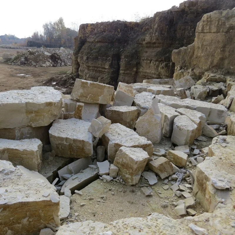 Large fallen limestone blocks and rubble at a quarry site with excavated earth and rocky cliffs in the background.