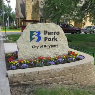 Sign for Perro Park in Bayport, New York, with colorful flowers in a landscaped bed.