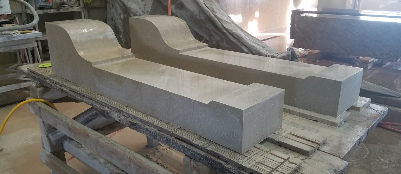 Two large, rectangular stone blocks with curved, carved tops, resting on a wooden workbench in a workshop.