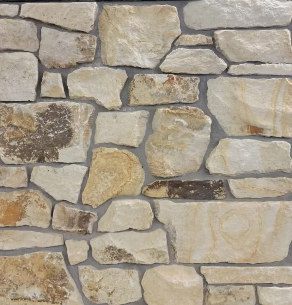 Close-up of a beige stone wall with irregularly shaped stones and mortar joints.