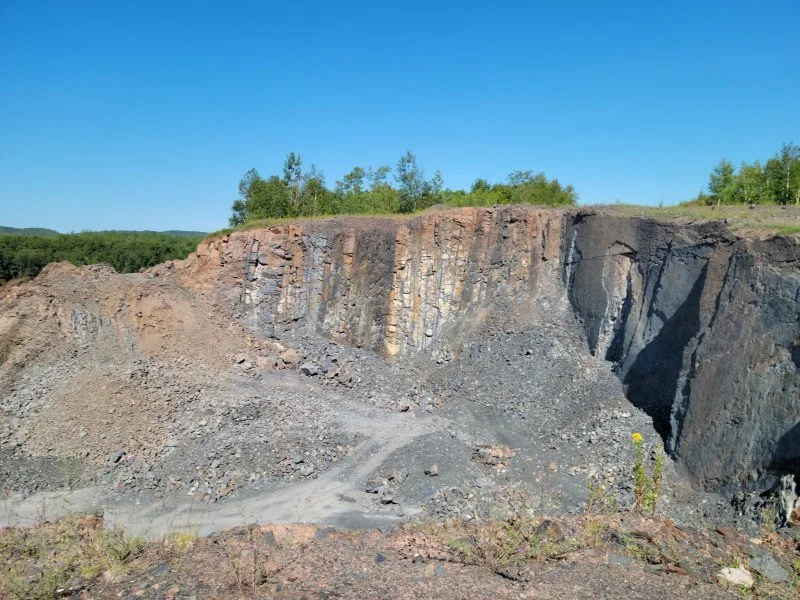 A quarry with exposed layered rock formations and a dirt path leading into the excavation site.