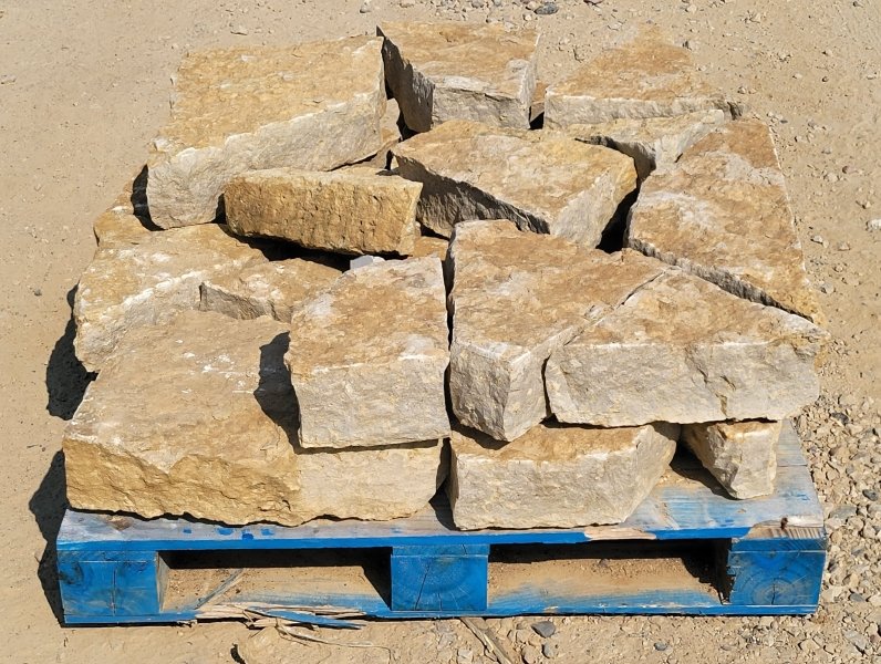 A pallet with uneven, rough-cut beige stone bricks stacked on top.