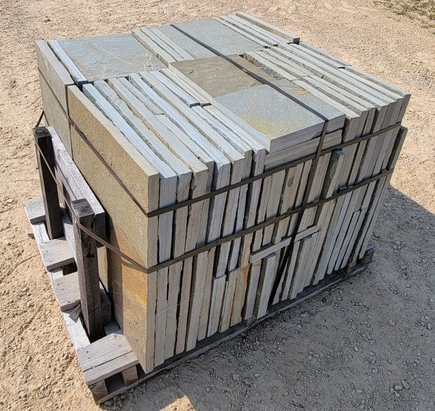 Stack of concrete and wooden paving stones secured with black straps on a wooden pallet outdoors.