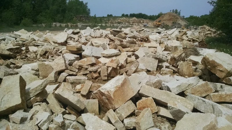 A construction site with large rocks and rubble scattered across the ground, and trees in the background.