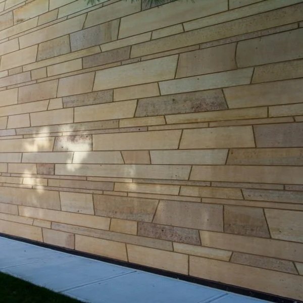 Exterior beige stone brick wall with a small section of sidewalk and a shadow of clouds.