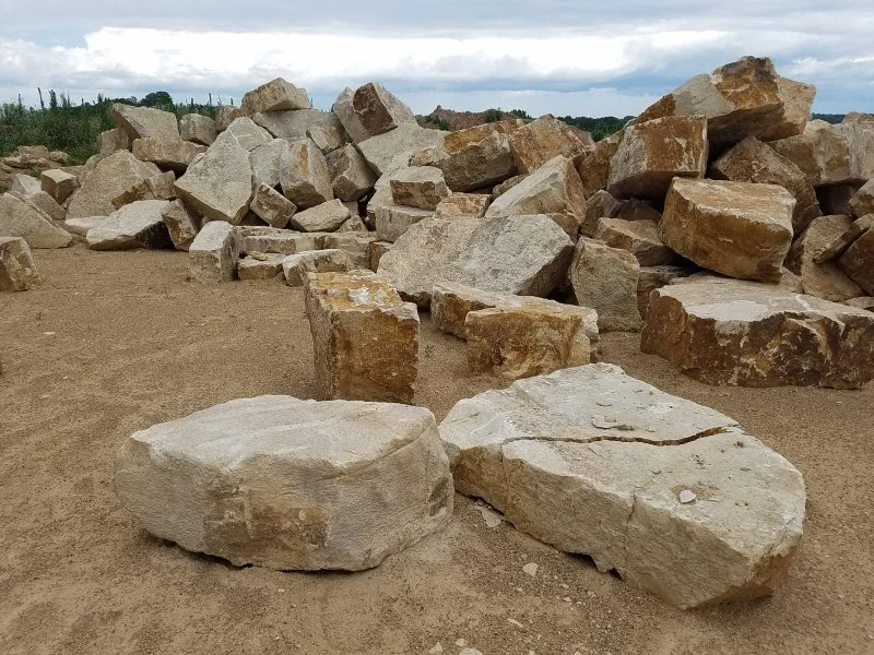 Large rocks and boulders scattered on dry ground with a cloudy sky in the background.
