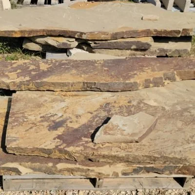 Stacked flat stone tiles outdoors, some broken, weathered, and uneven.