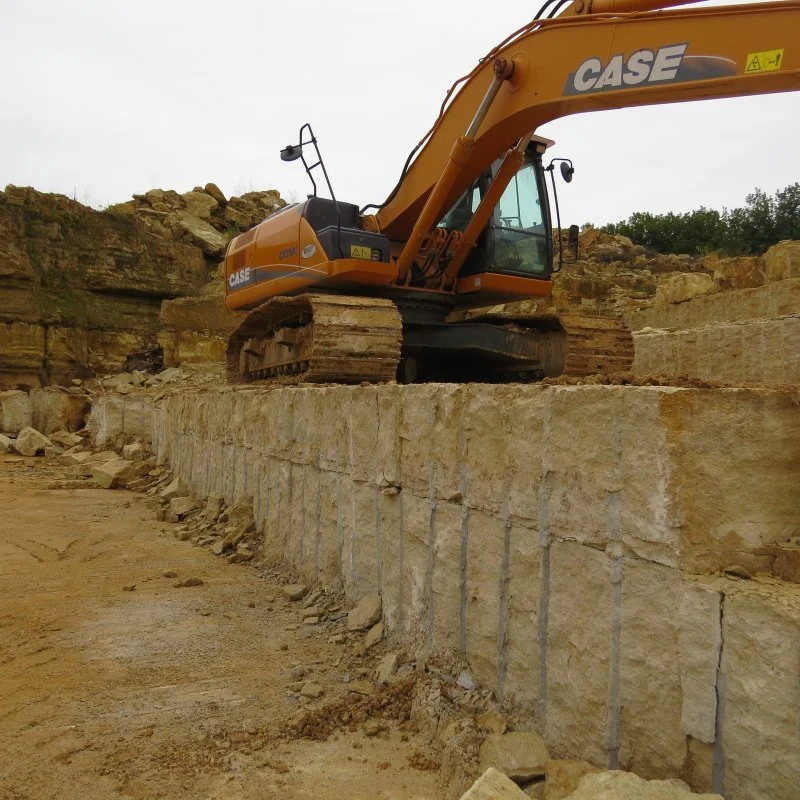 Yellow CASE excavator positioned on a stone ledge during construction, with exposed layered rock formations in the background.