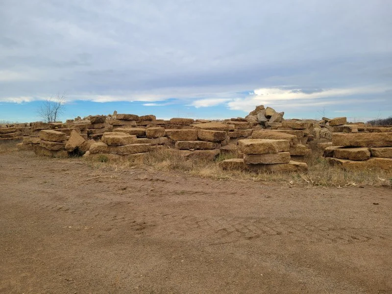 A rural scene with a dirt road and a low stacked stone wall under a cloudy sky.