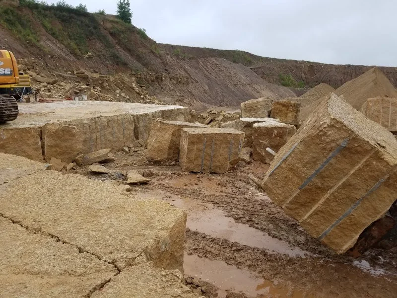 Large rectangular stone blocks on muddy ground at a construction or excavation site, with a bulldozer partially visible on the left and a hillside in the background.