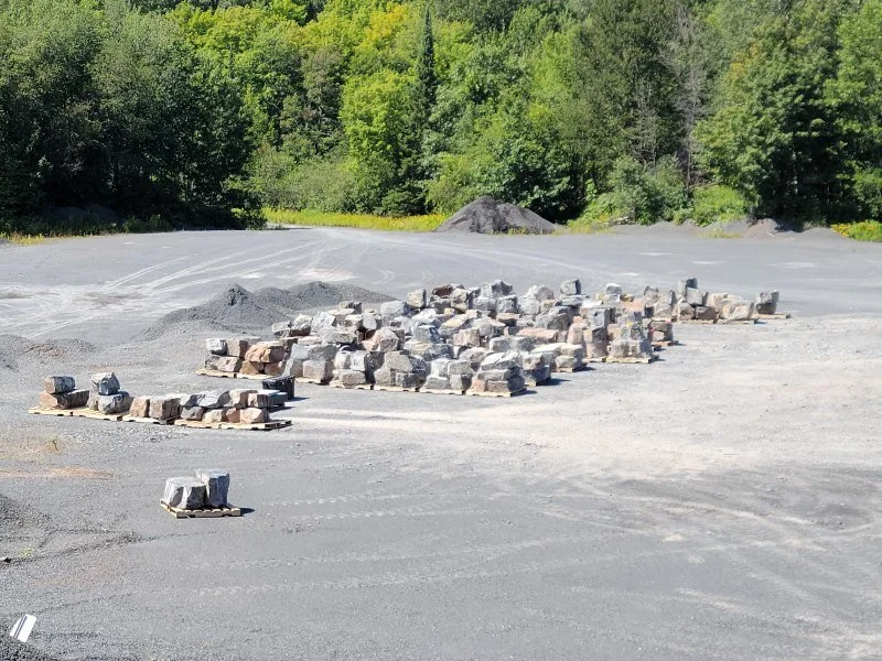 Stacked rocks and gravel on a gravel road surrounded by trees.