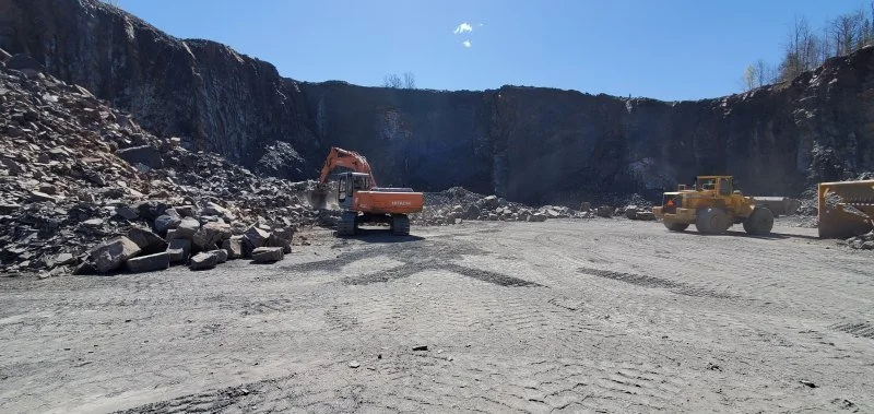Construction site with an excavator and a wheel loader in a quarry surrounded by rocky walls.
