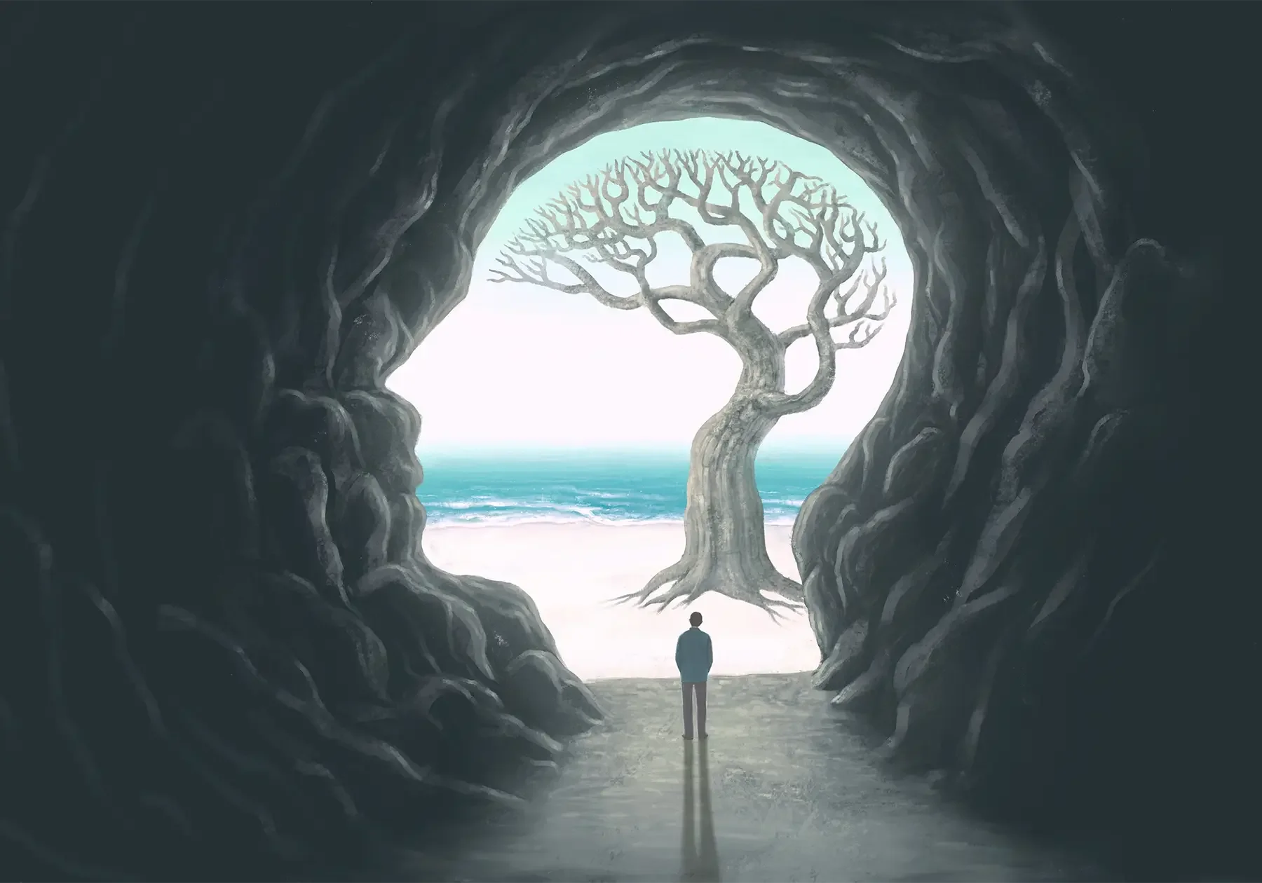 A person standing at the entrance of a dark cave is looking at a large, leafless, twisted tree standing on a beach with the ocean in the background.