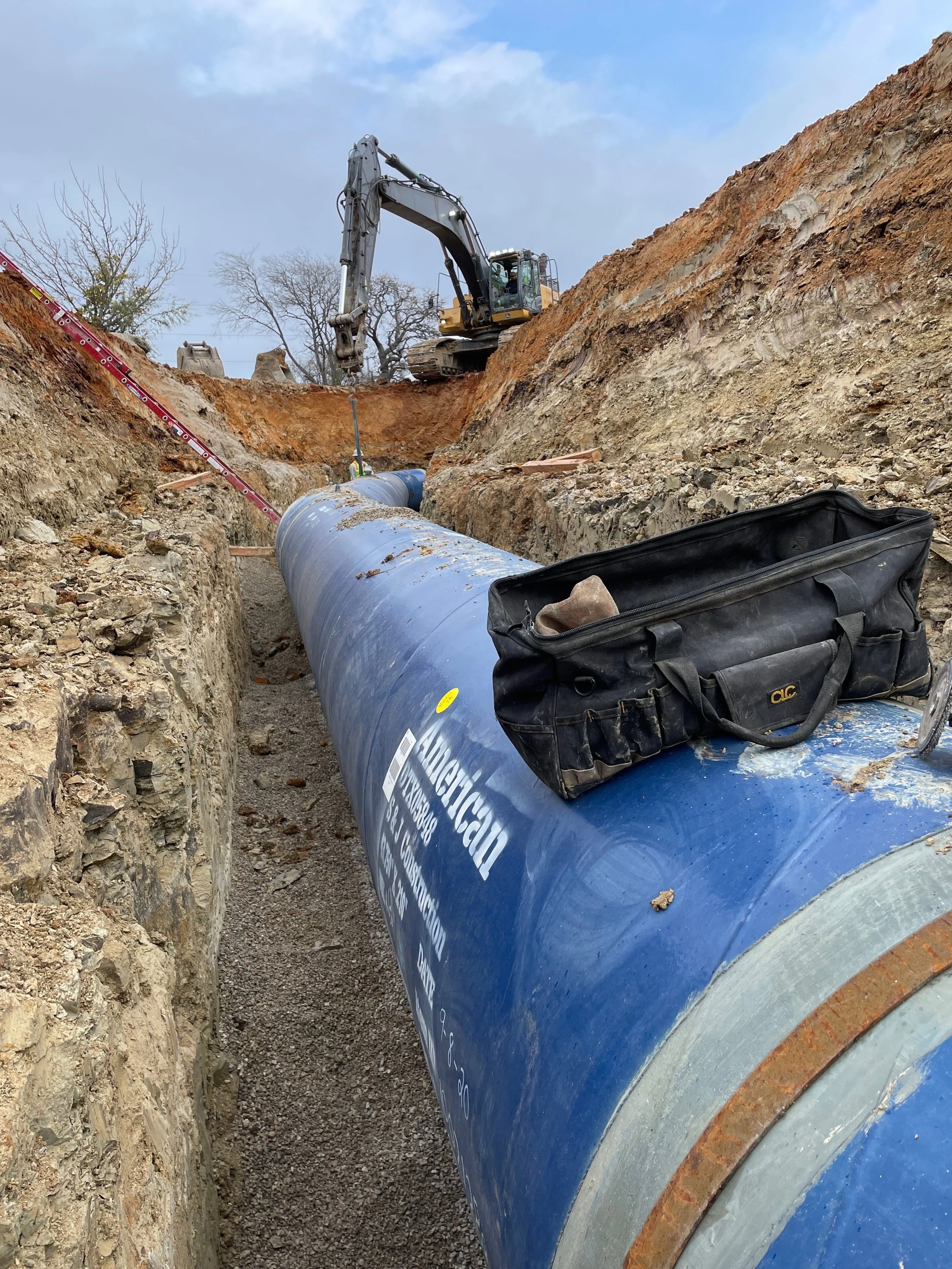 Construction site with large blue pipe in trench and excavator working on upper edge