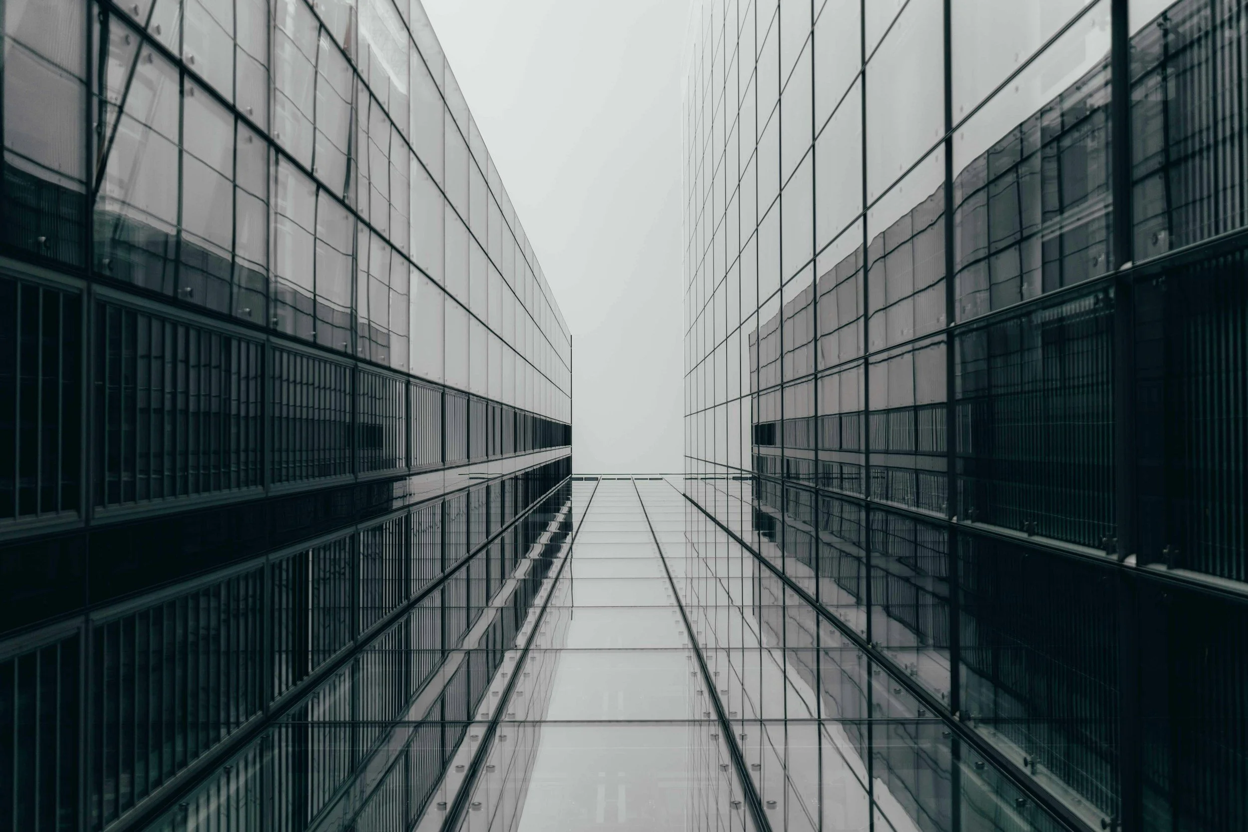 Two tall modern skyscrapers with reflective glass facades. The buildings are close together, looking upwards towards the cloudy sky.