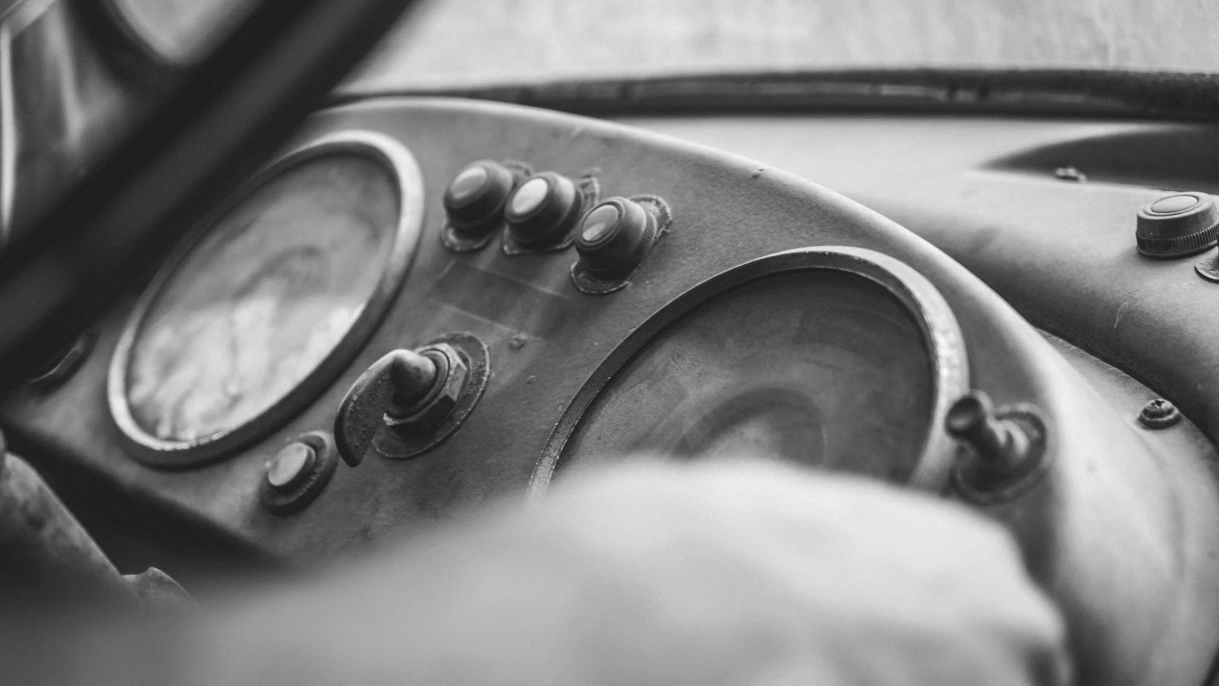 Black and white photo of an old, weathered vehicle dashboard with circular gauges and switches.