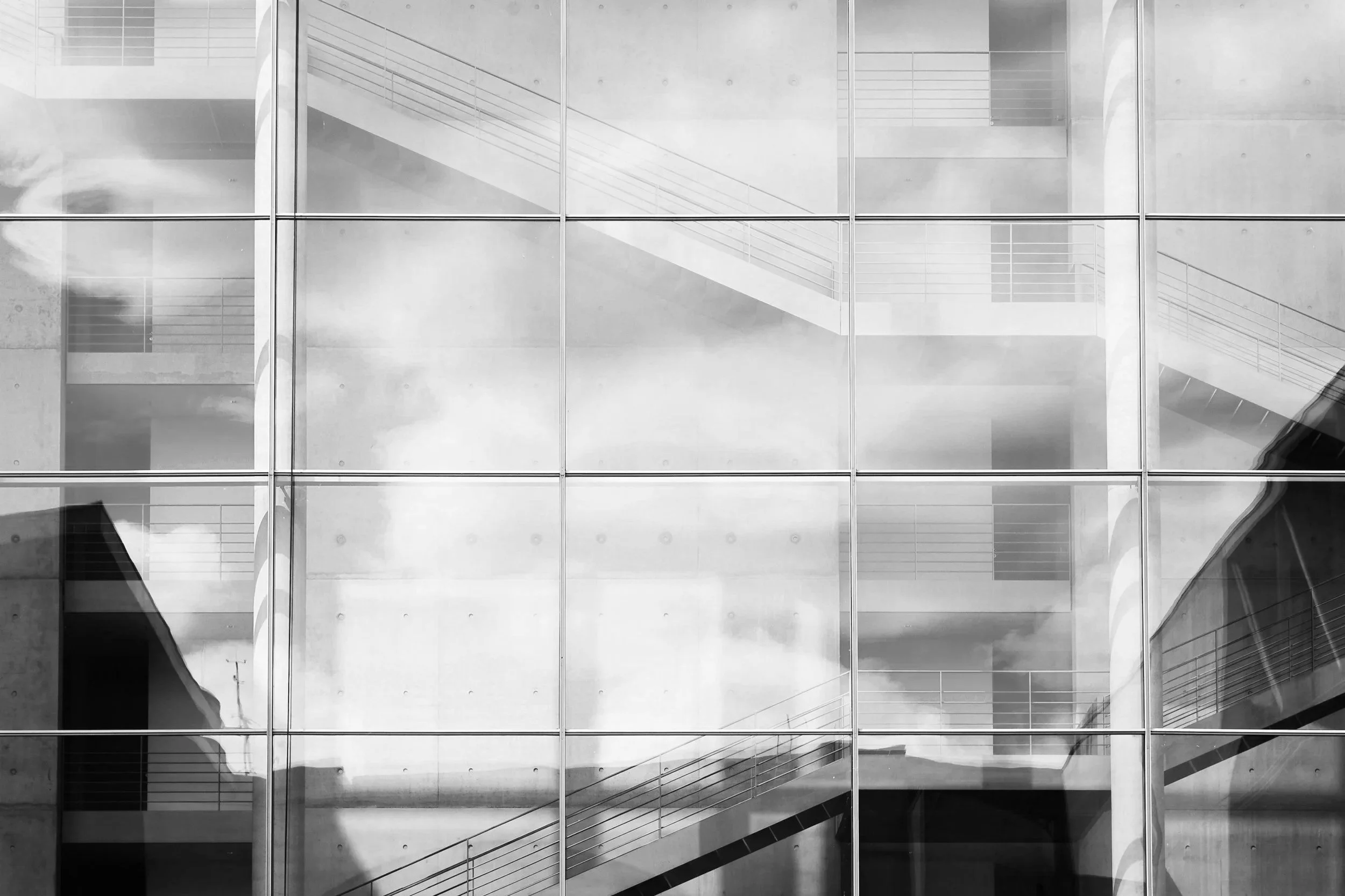 Reflection of a building with stairs and sky visible through large glass windows