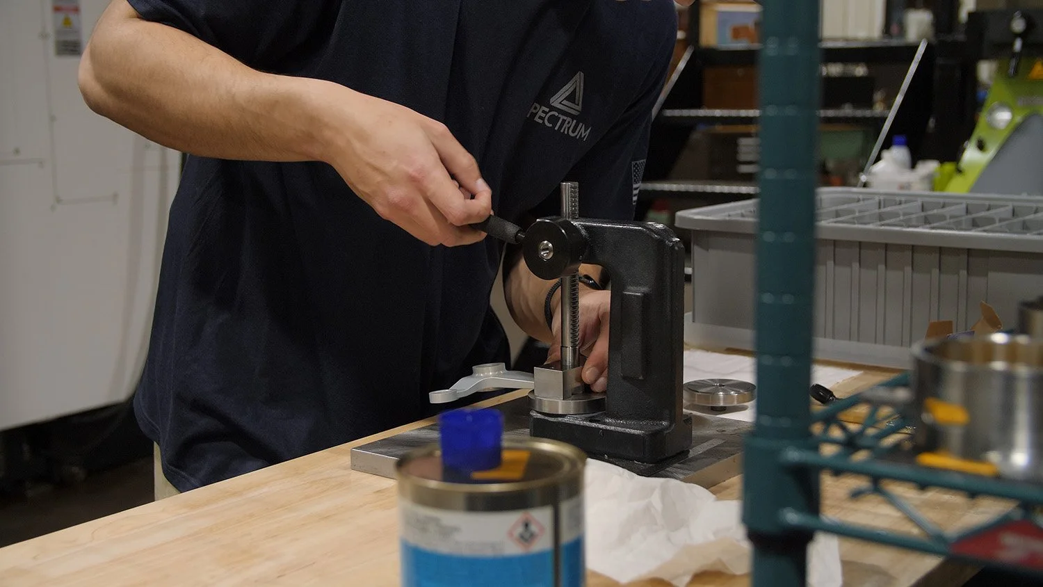 aerospace machinist jobs Ohio A person wearing a black shirt using a small black press to press or stamp something on a white surface, on a workshop or laboratory bench.