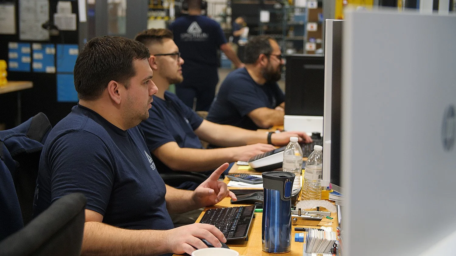 aerospace machinist jobs Ohio Four men working on computers in an industrial workspace, with shelves and boxes in the background.