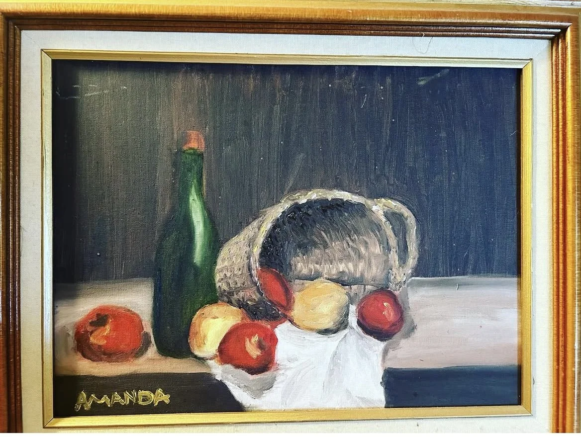 A still life painting of fruits and a bottle on a table, including apples, pears, a watermelon, and a green bottle, signed 'Amanda' in the lower left corner.