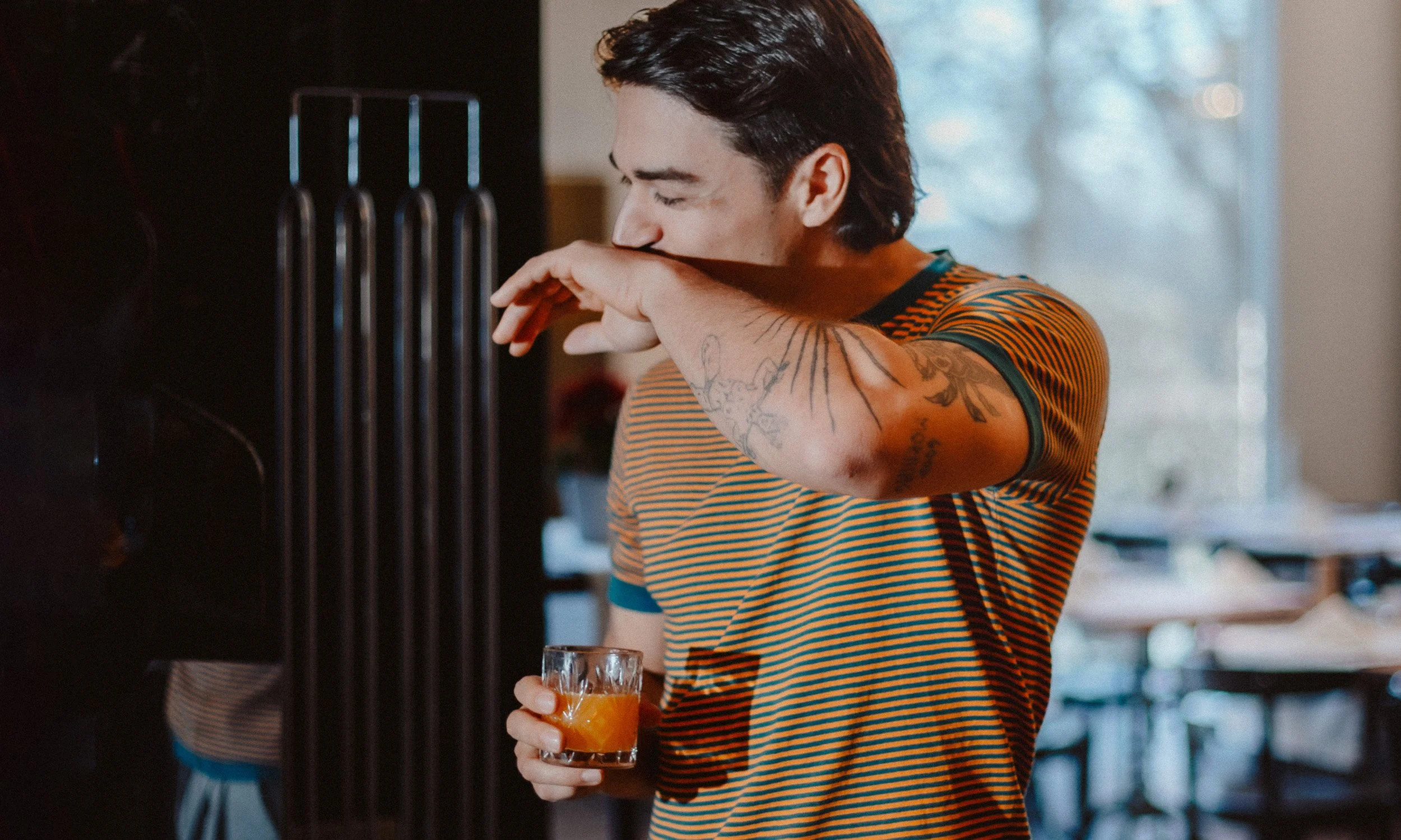 Junge mit Tattoos trinkt Whiskey aus einem Glas in einer Bar.