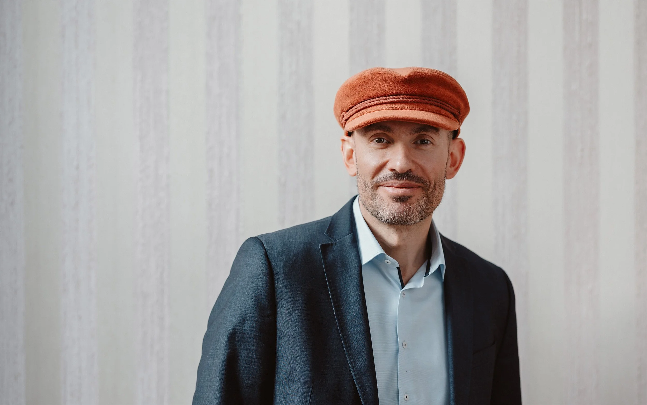 Mann im Anzug mit roter Mütze vor einer neutralen wand