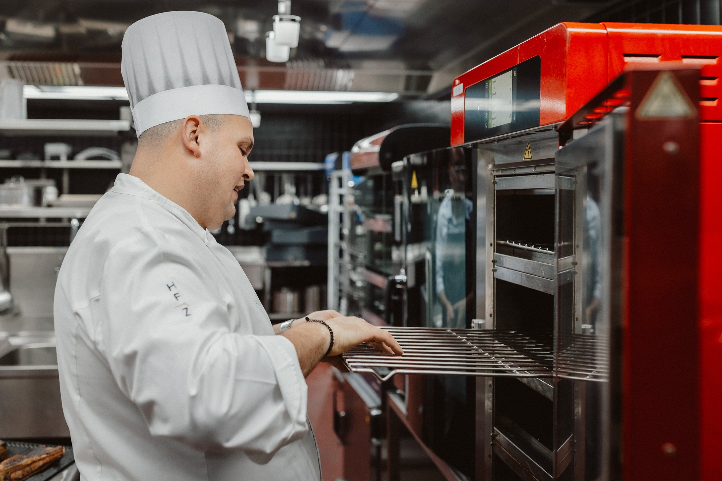 Ein Koch in Weiß sichert einen Ofen in einer professionellen Küche.