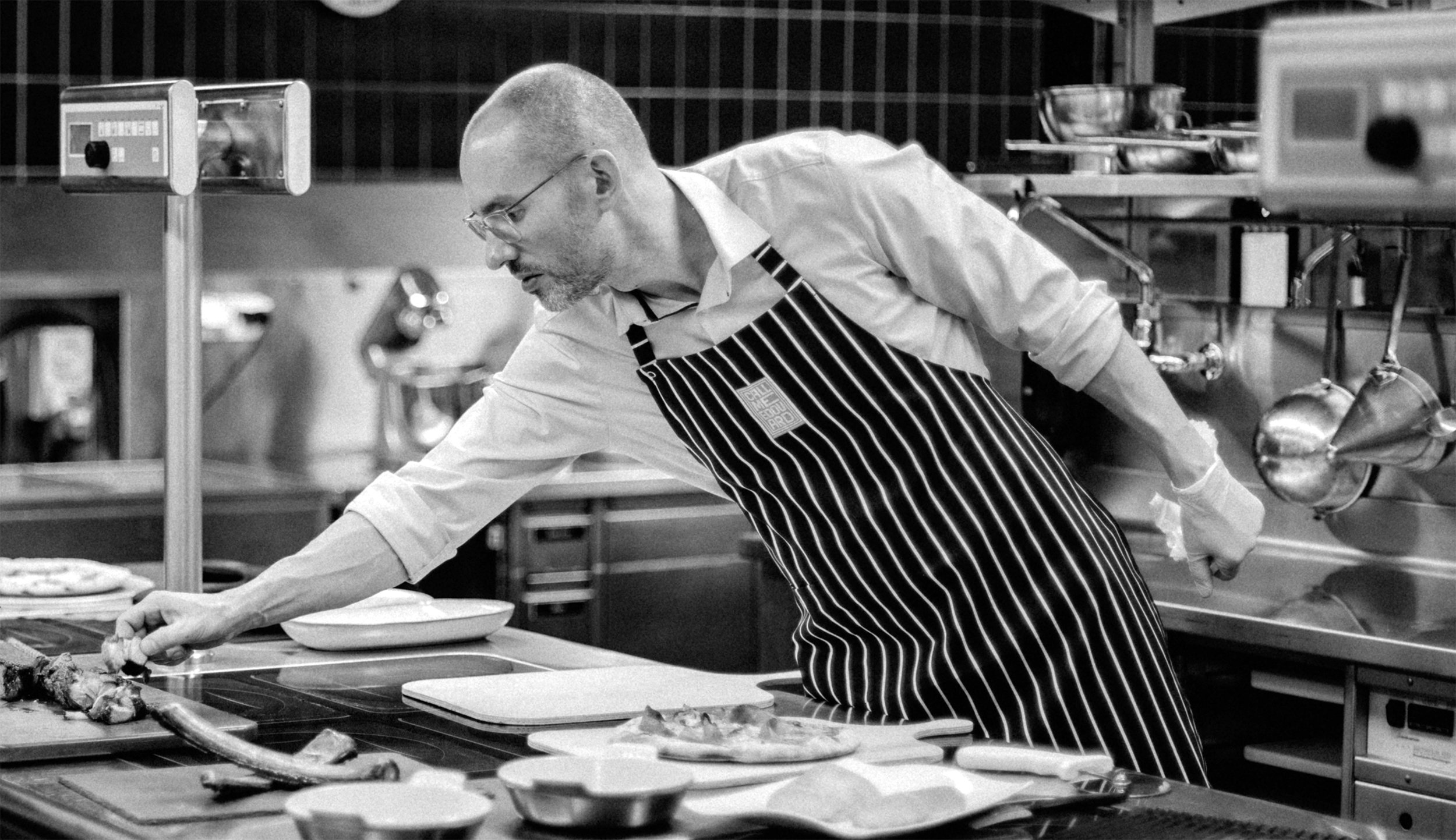 Ein Mann in Kochschürze bereitet in einer professionellen Küche Nahrung zu.