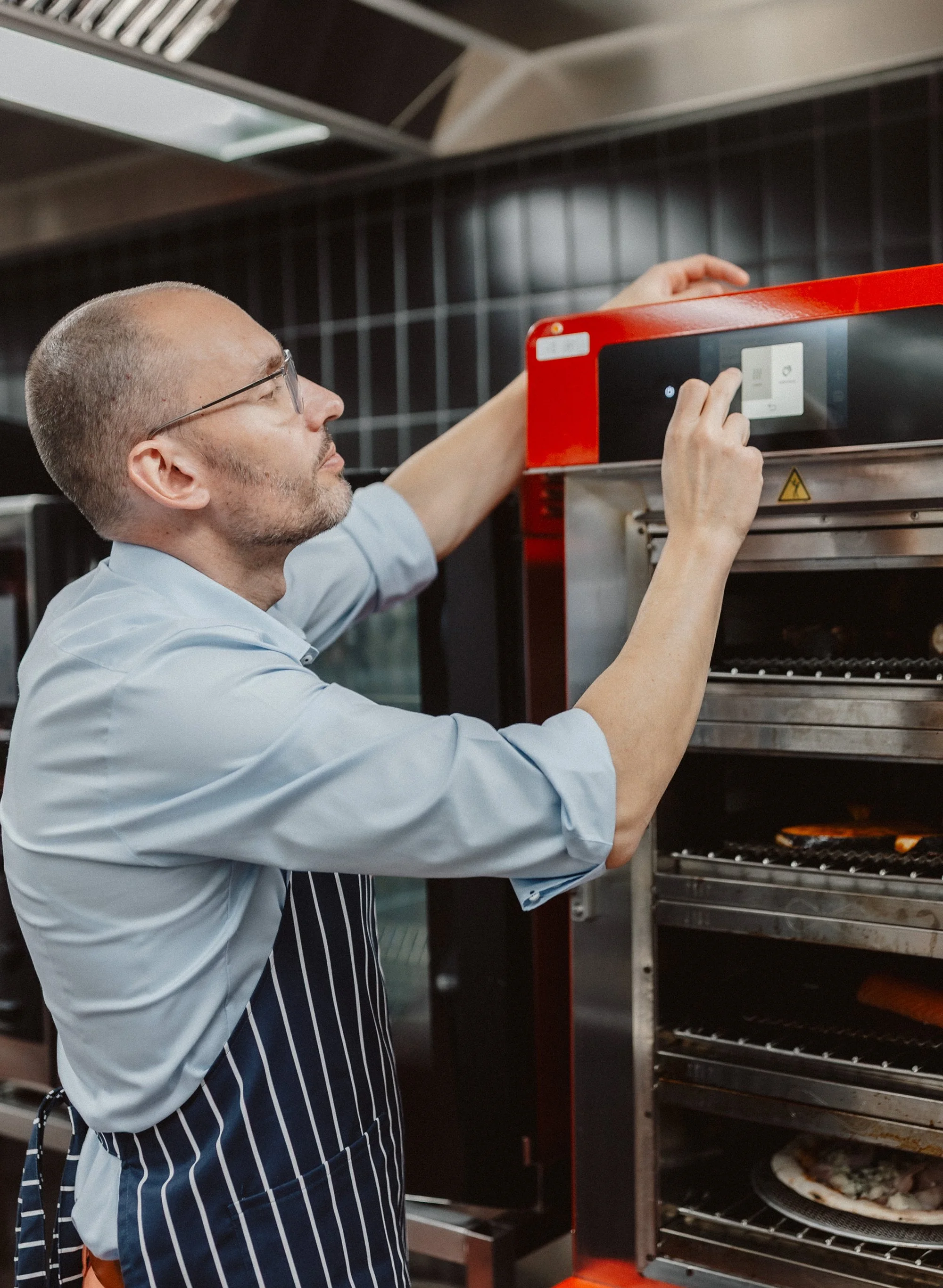 Ein männlicher Koch überprüft die Temperatur eines Backofens in einer Gastronomieküche.
