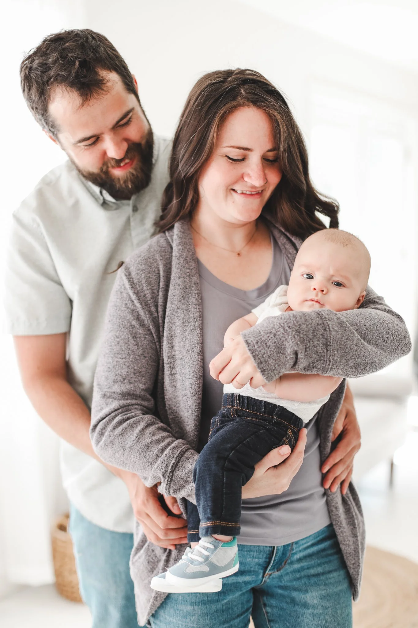 A happy family with a woman holding a young baby and a man leaning in close, all smiling indoors.