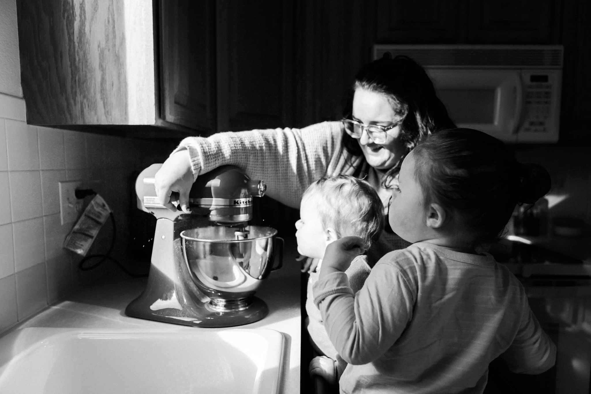 A woman cooking with two children in a kitchen, using a stand mixer.