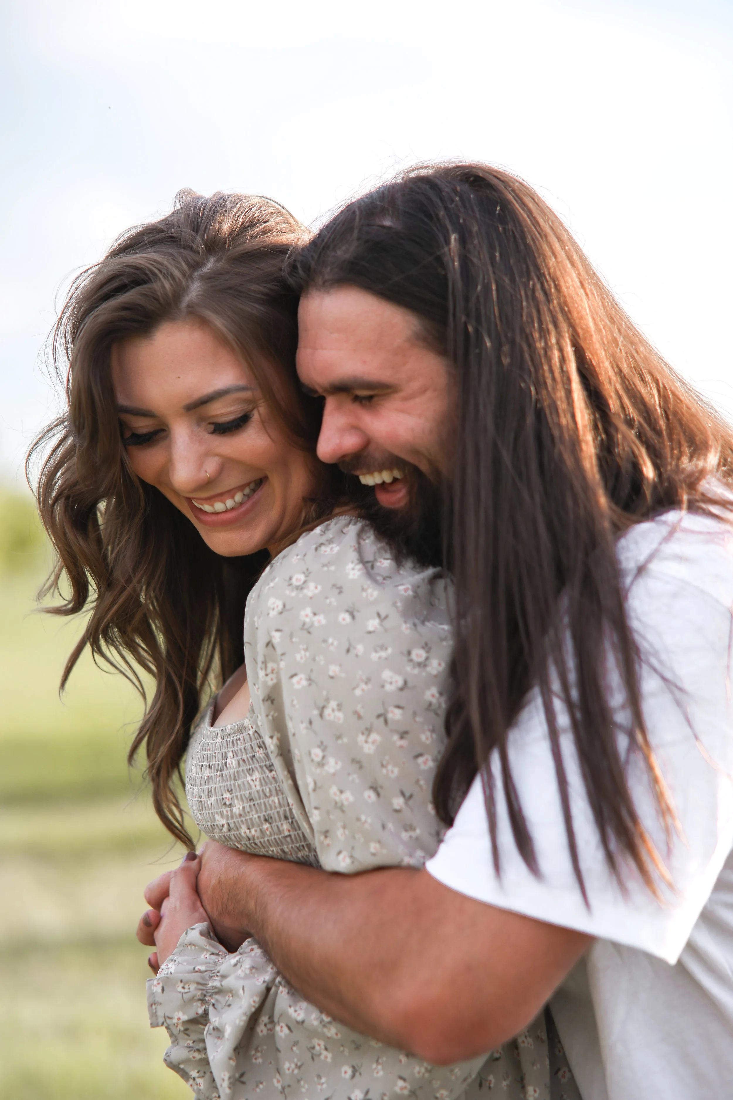 A happy couple embracing outdoors during daytime, smiling and looking at each other.