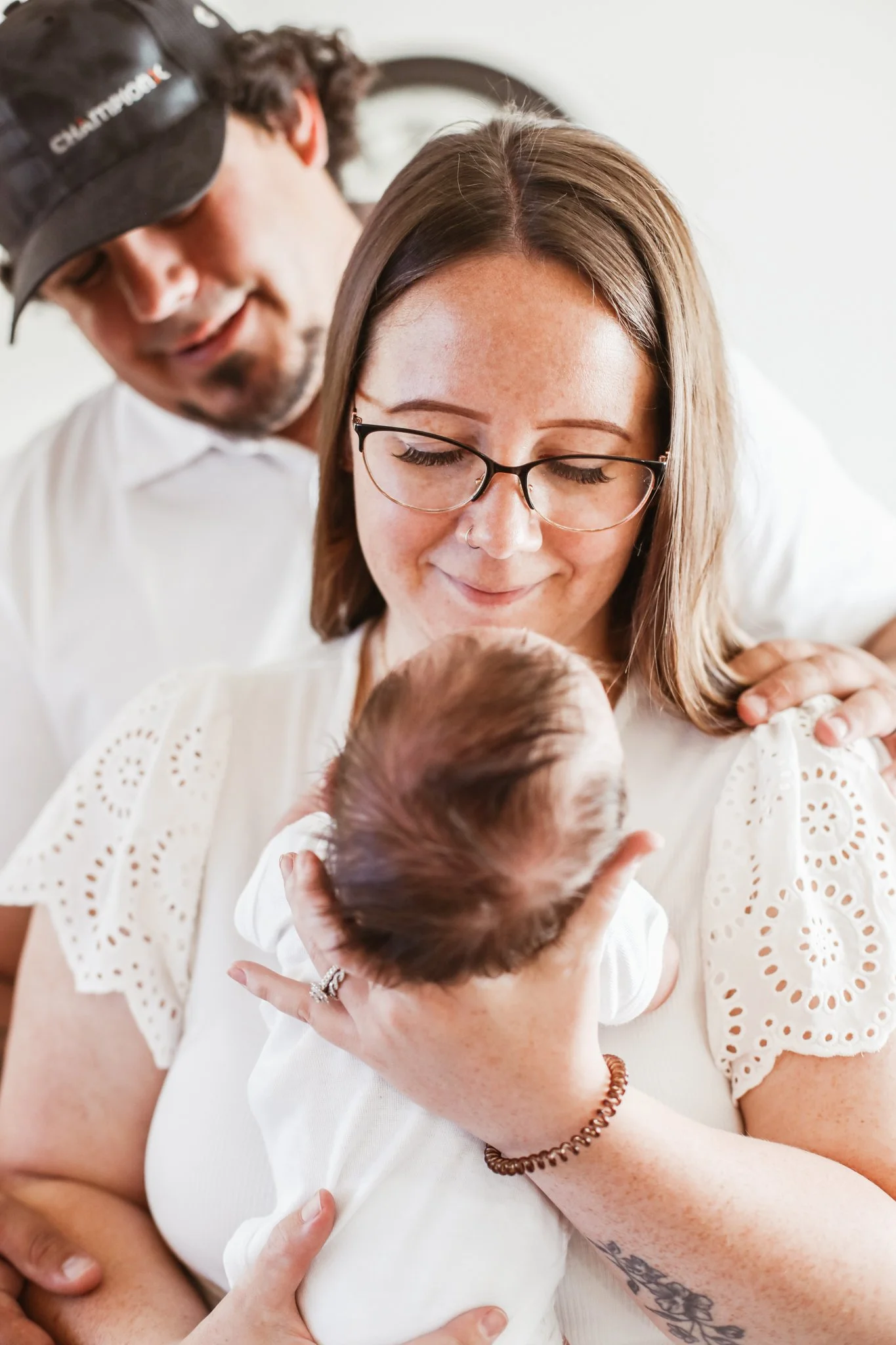 A woman with glasses holding a newborn baby, with a man standing behind her, smiling and looking at the baby.