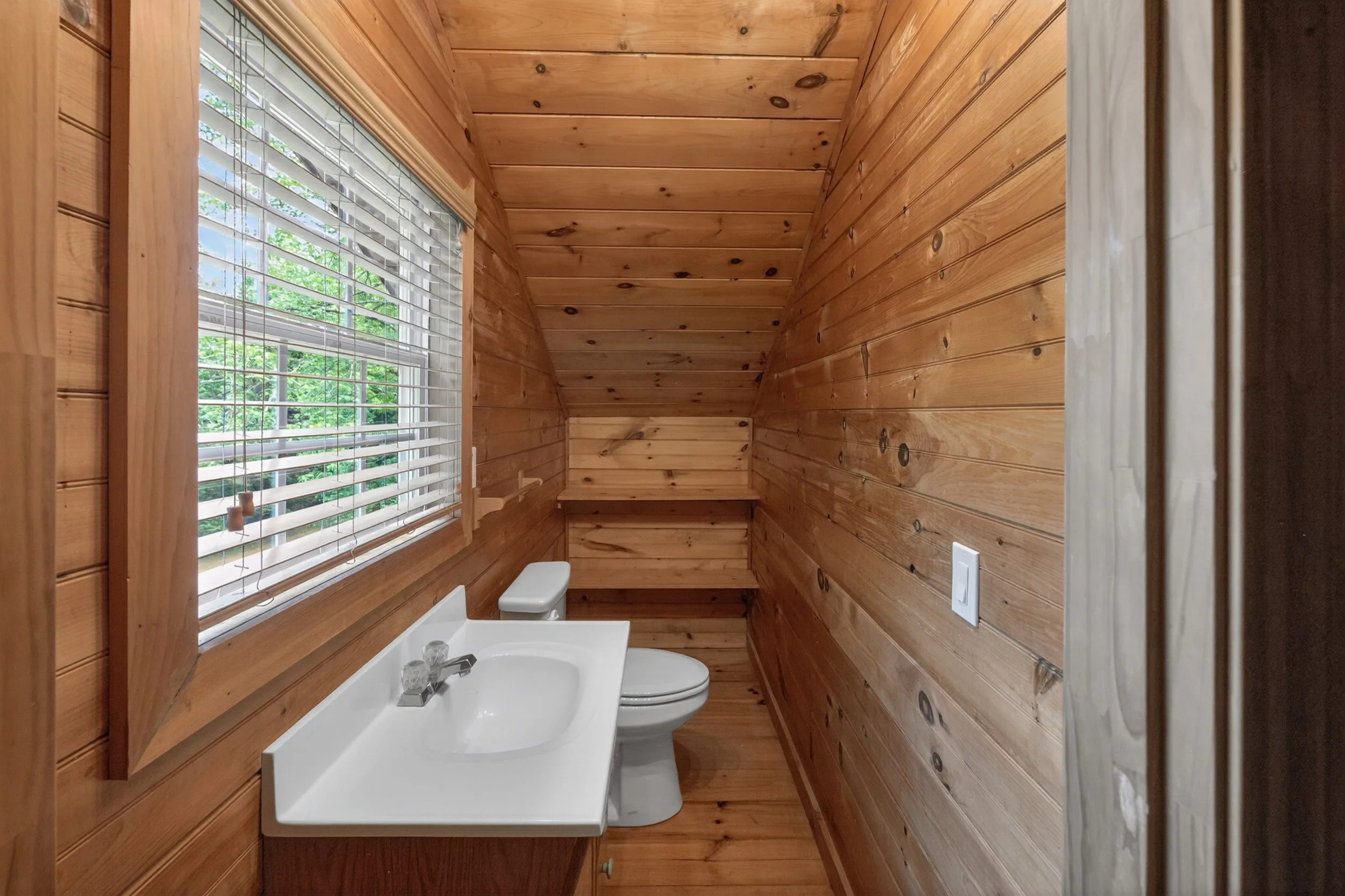 Wood-paneled bathroom with window, sink, and toilet.