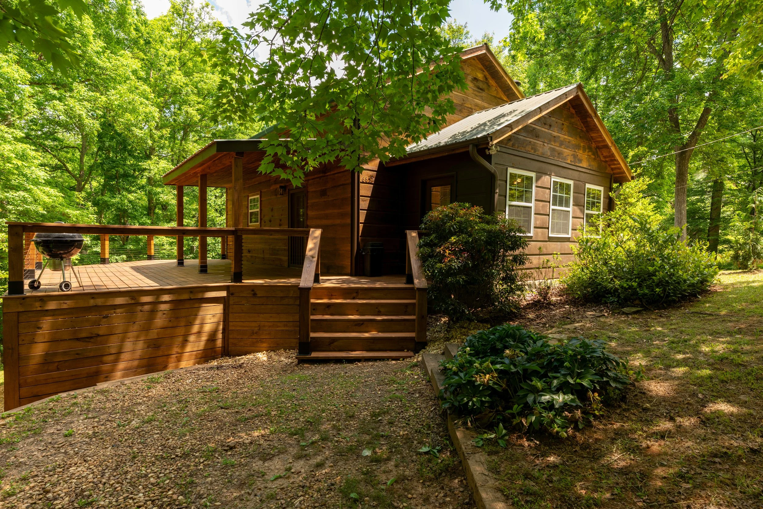 Wooden house with deck and green trees in a forested area.
