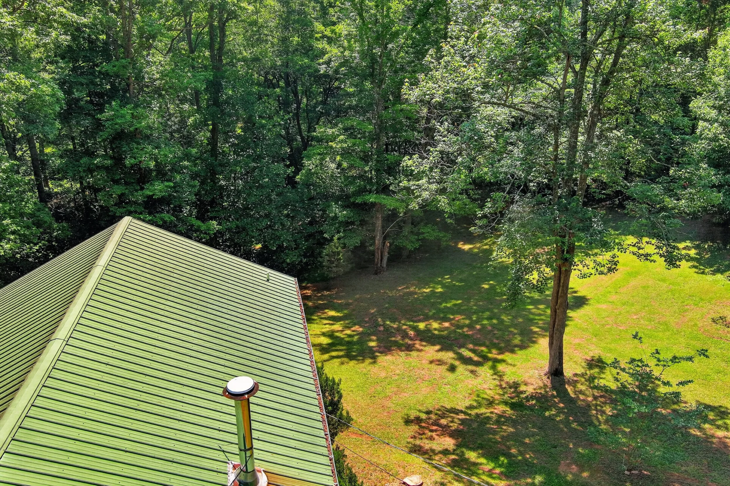 A green metal roof seen from above with a large tree and a grassy yard in the background.