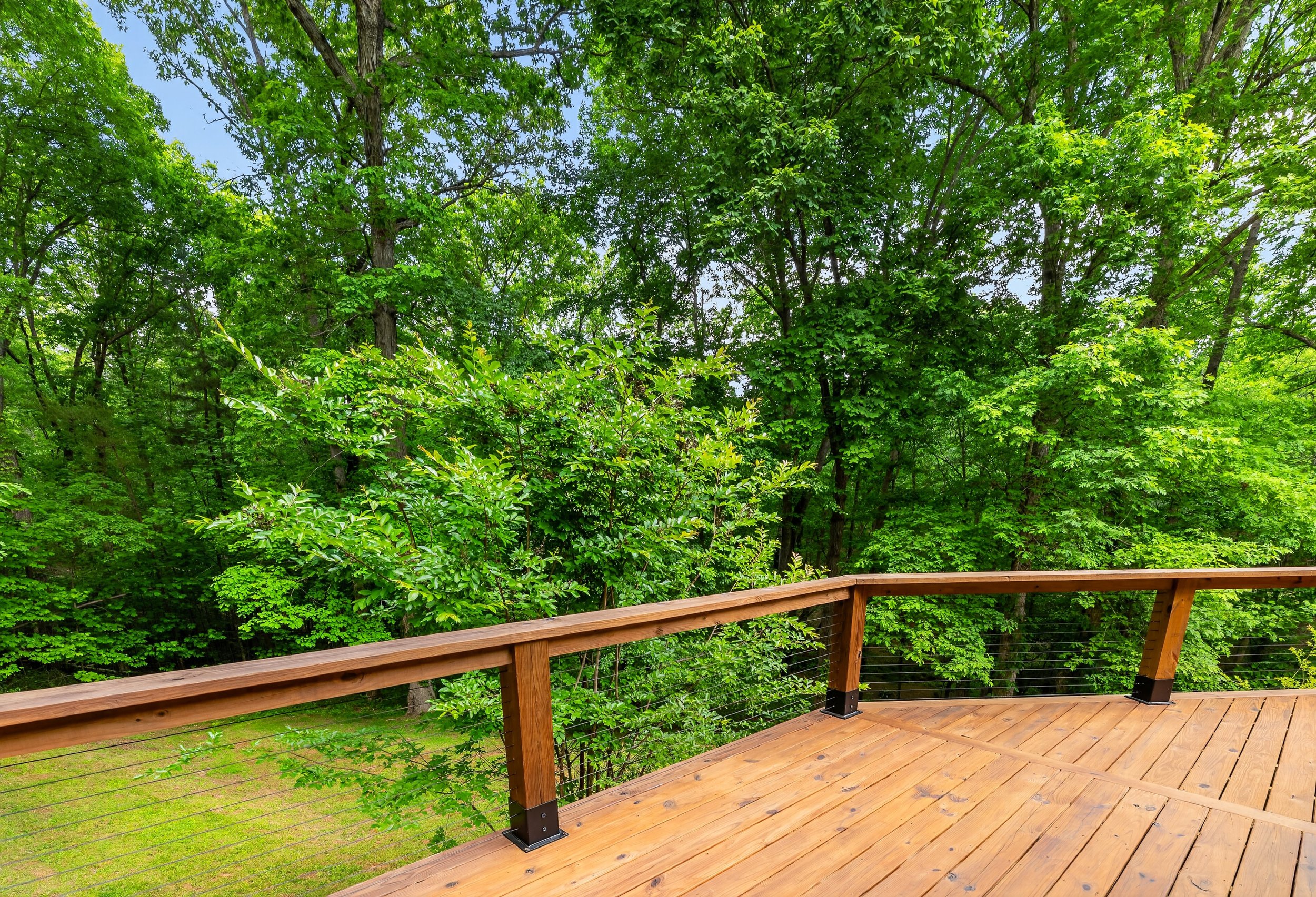 Wooden deck overlooking a lush green forest with tall trees and bright green leaves.