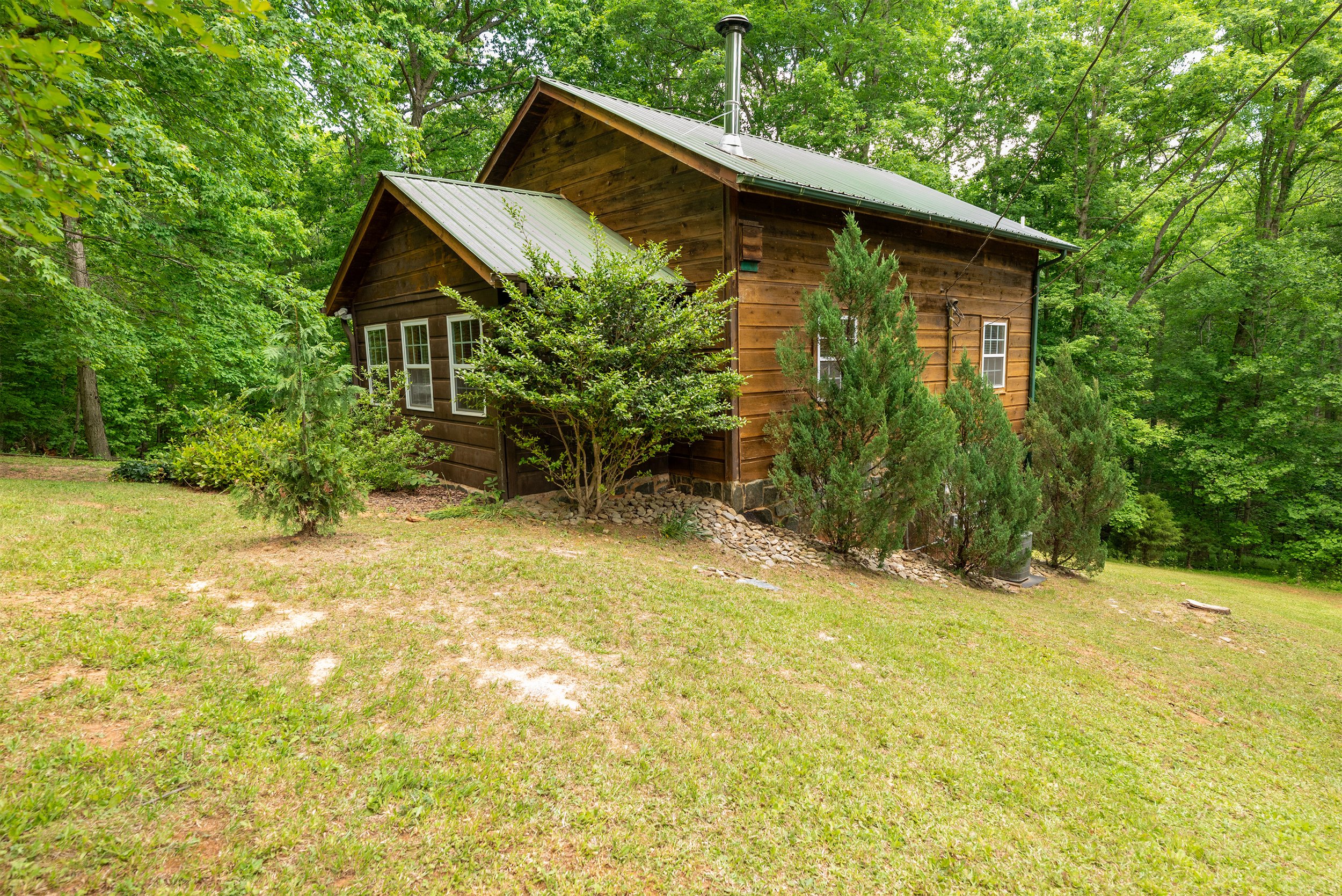 A rustic wooden house with a metal roof, surrounded by lush green trees and bushes.