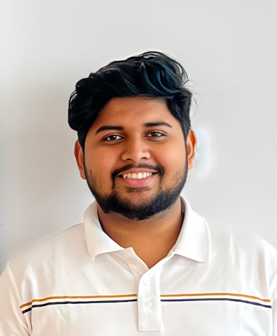 Portrait of a young man with dark hair, beard, and mustache, smiling, wearing a white polo shirt with thin horizontal stripes, standing against a plain white background.