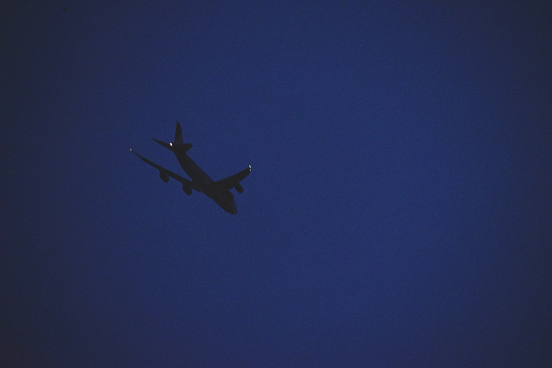 Silhouette of a large commercial airplane flying against a dark blue evening sky with a few distant lights on its wings.